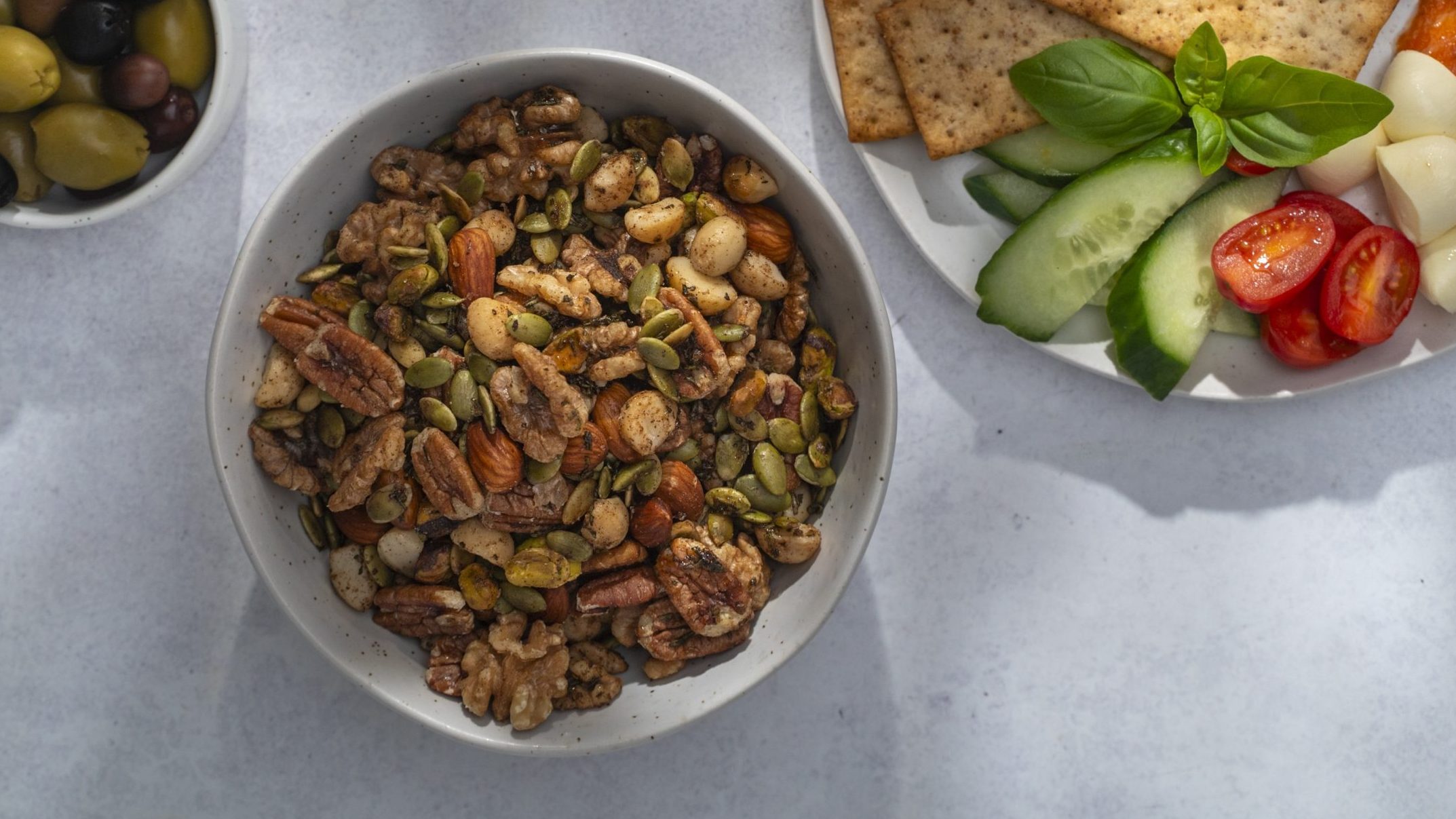 Roasted mixed nuts and seeds in a bowl, and a plate of crackers and vegetables.