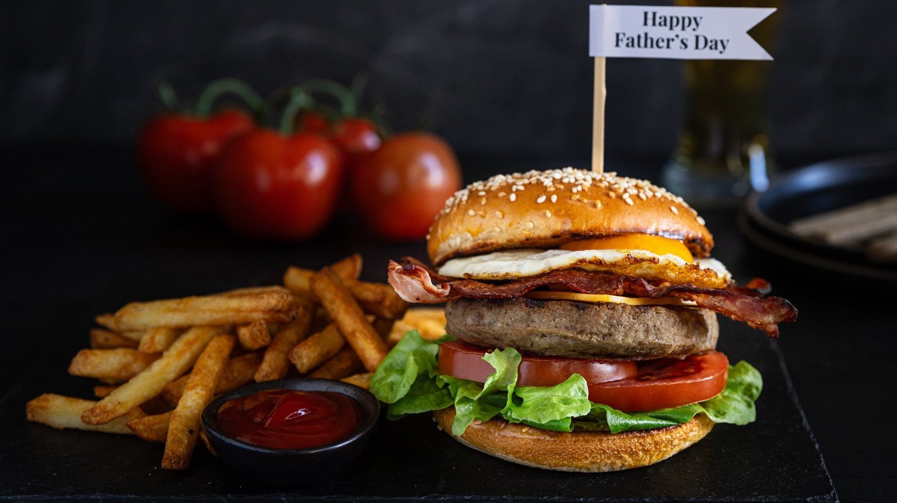 Side view of a beef burger with Father's Day message. Chips, tomatoes and beer.