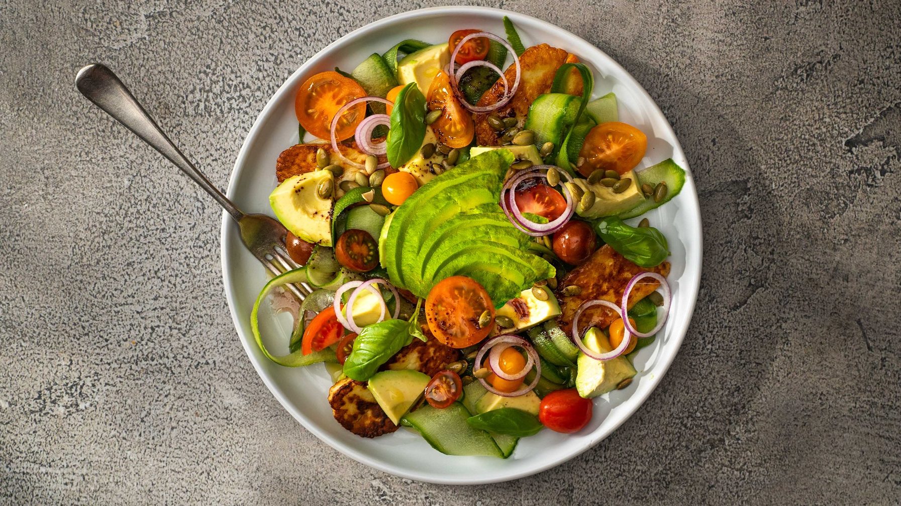 Topdown view of a tomato and avocado salad in a white round bowl with a fork.