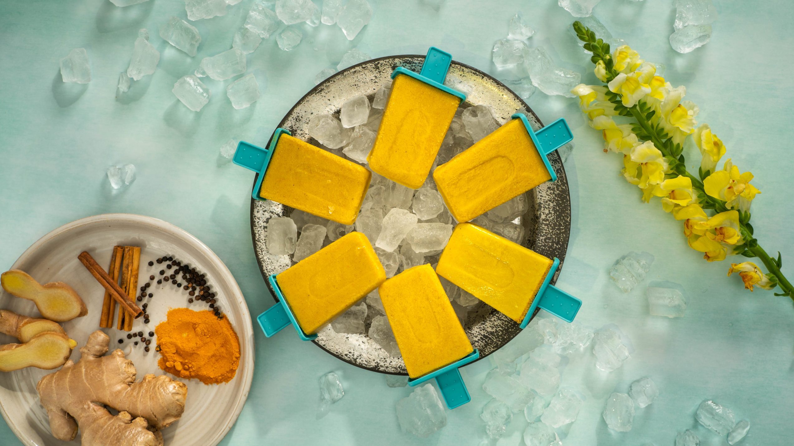 Yellow ice blocks on a plate srounded by ice cubes, flower and spices.