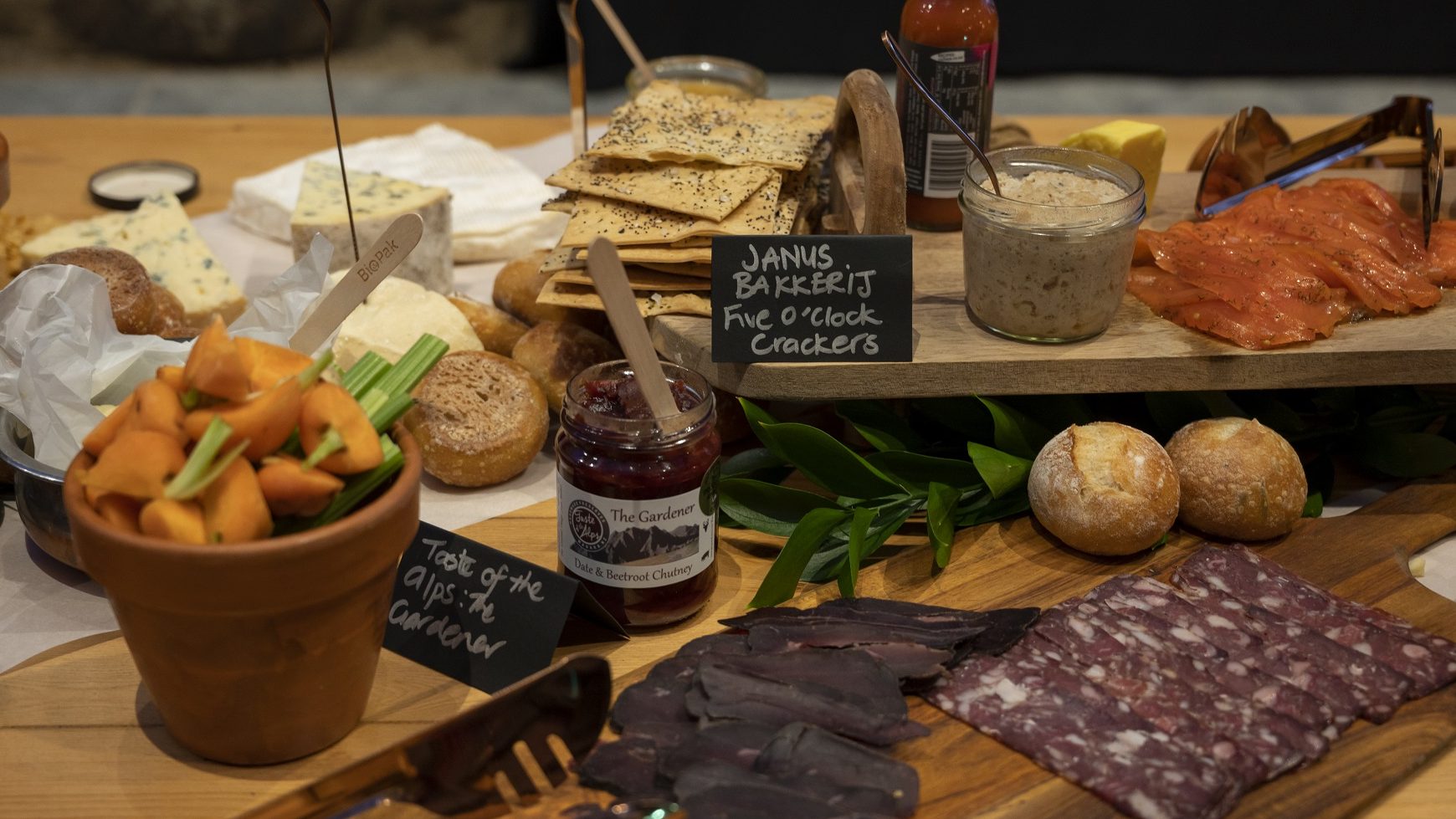 A selection of fine NZ-made delicacies featuring cheese, charcuterie, dips, smoked salmon, crackers etc...displayed on a wooden table.