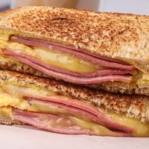 Two halves of grilled ham and cheese sandwich stack on a paper lined board.