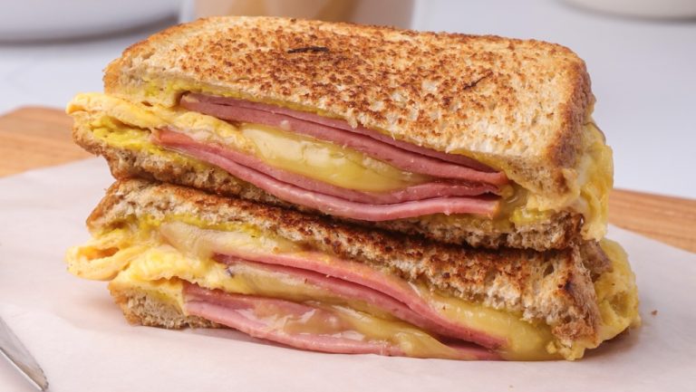 Two halves of grilled ham and cheese sandwich stack on a paper lined board.
