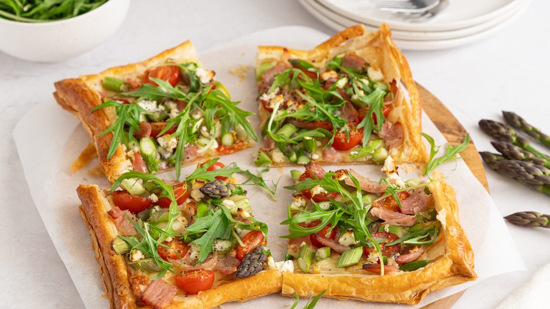 A square pie cut into four slices with colourful fillings on a board.