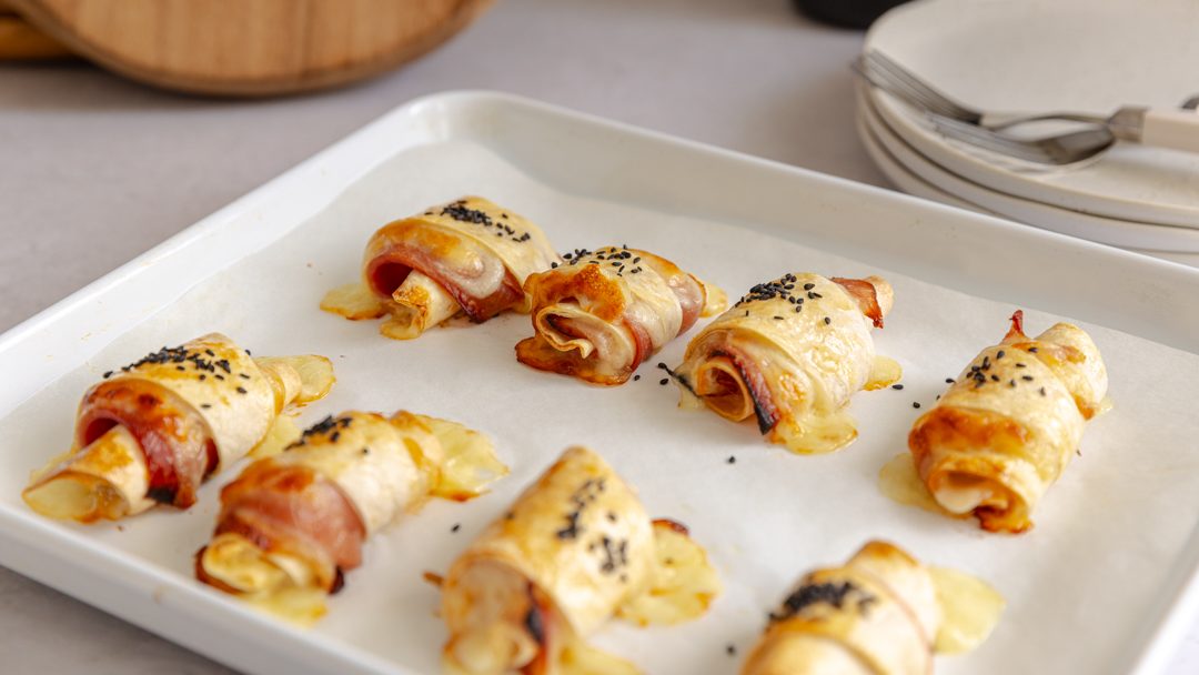 A tray of baked bread pieces with ham and cheese rolled inside.