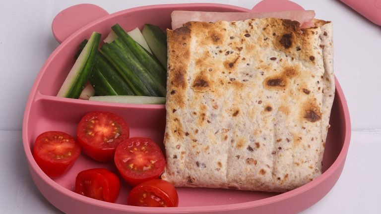 A toasted folded wrap, cucumber sticks and cherry tomatoes in a teddy bear shaped pink lunchbox.