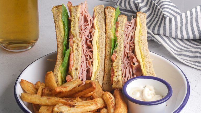 Ham, cheese and lettuce sandwiches on a plate with a bowl of mayonnaise and chips.