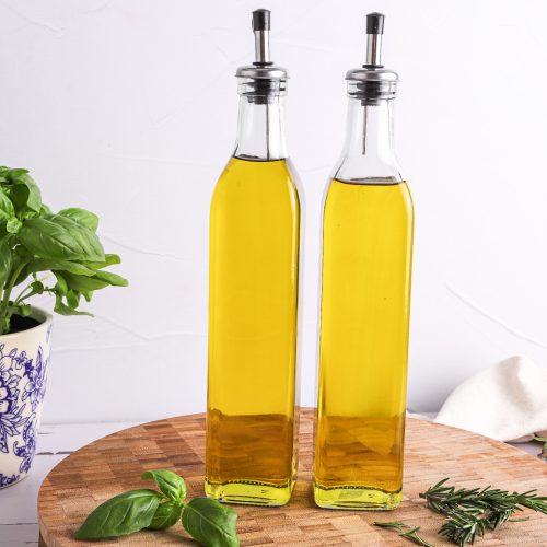 Two bottles of oil on round wooden board, a pot of basil at rear.