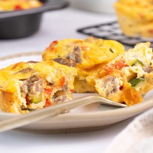 Two mini quiches on a plate, one is cut in halves showing colourful contents inside.