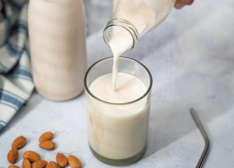 Pouring milk into a glass. A metal straw, almonds, a bottle of milk and green striped cloth