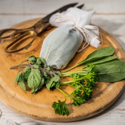 Some green herbs, a pair of scissors and a white parcel on round wooden board.