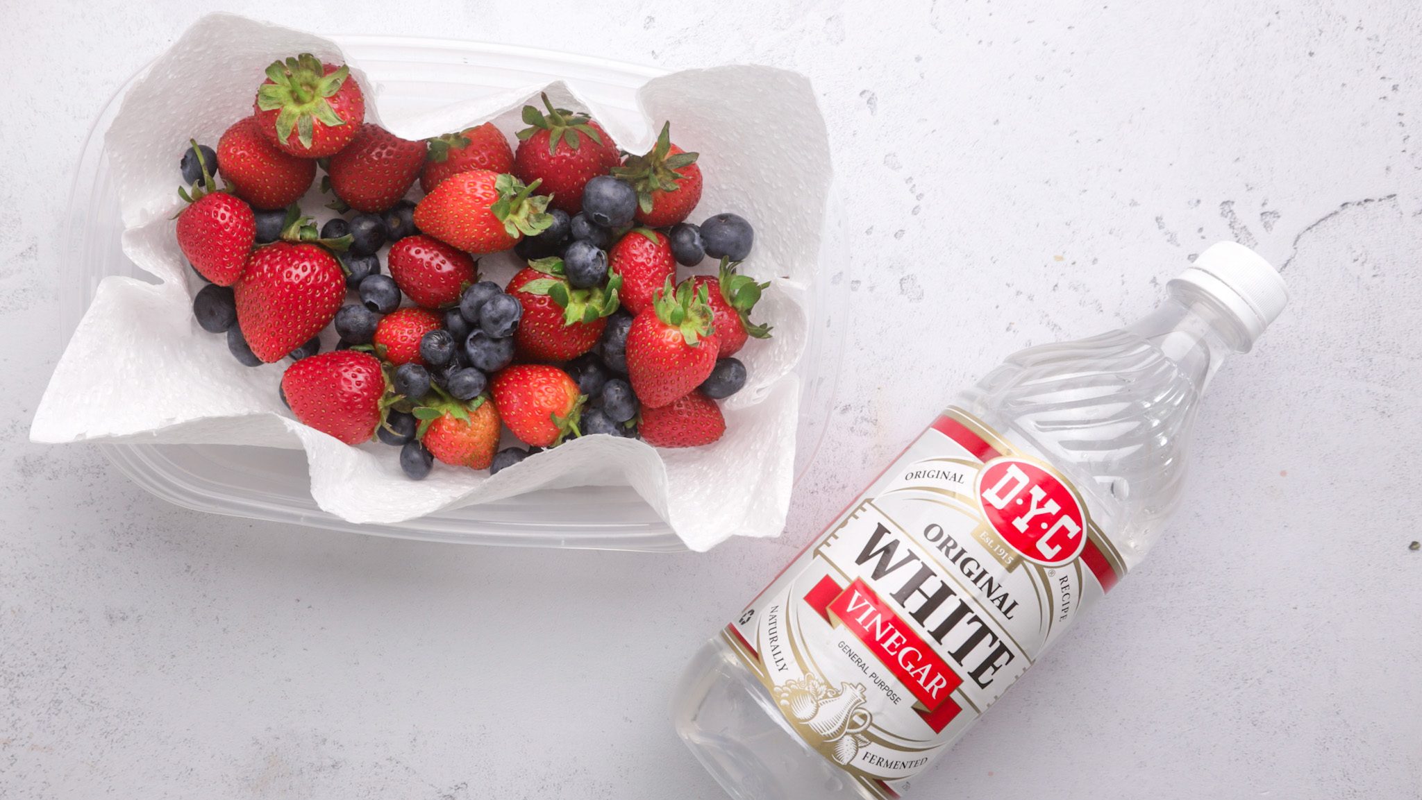 A paper lined container full of summer berries and a bottle of vinegar.