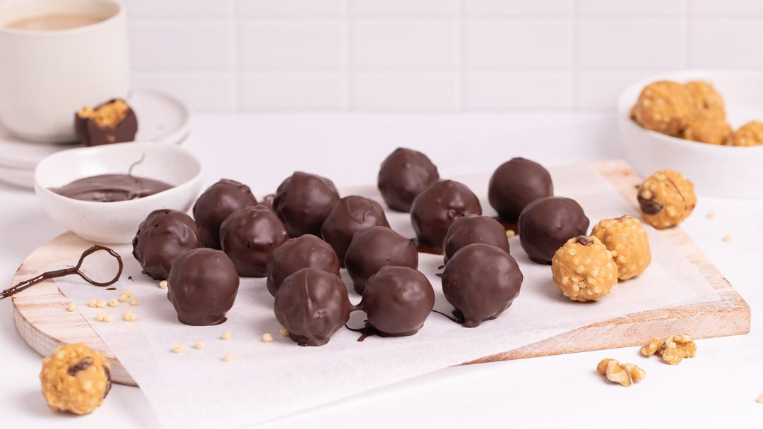 Chocolate covered balls and some uncovered on a board. A cup of milky coffee.