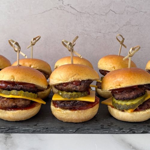 Several mini burgers with skewers lined up on a slate.