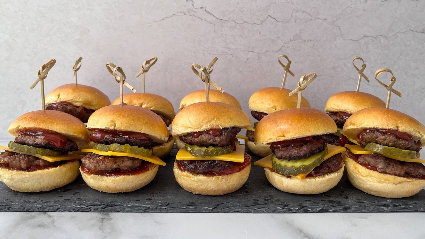 Several mini burgers with skewers lined up on a slate.