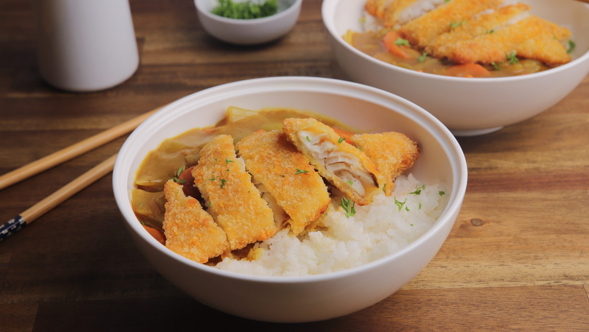 Crumbed fish on rice in a bowl with curry sauce .