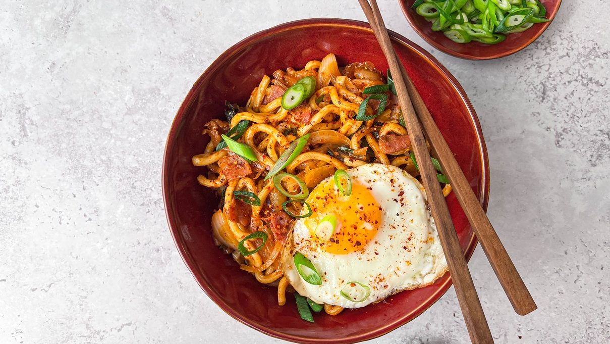 A bowl of noodles with a fried egg on top with a pair of chopsticks.