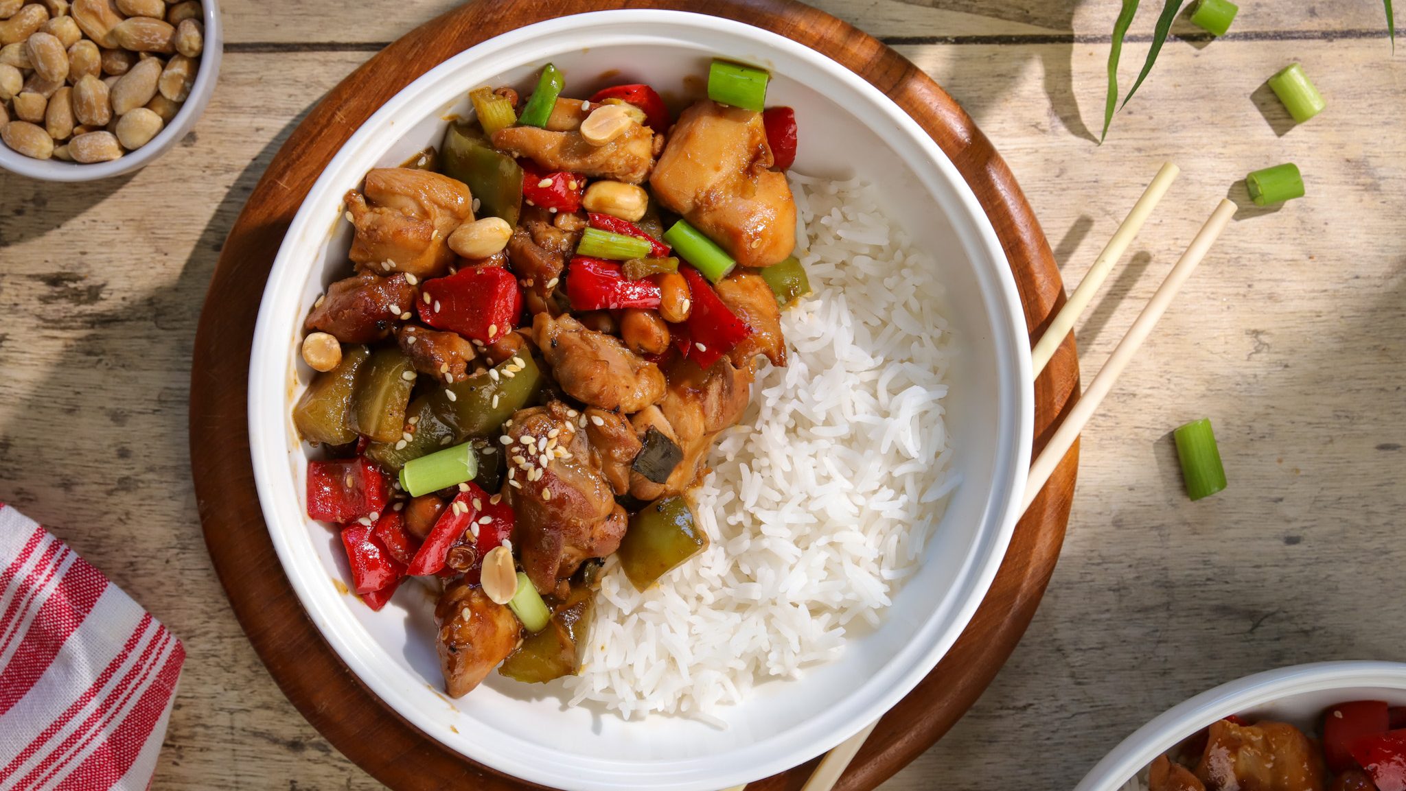 A bowl of white rice topped with chicken and vegetable stir-fry on half the side.