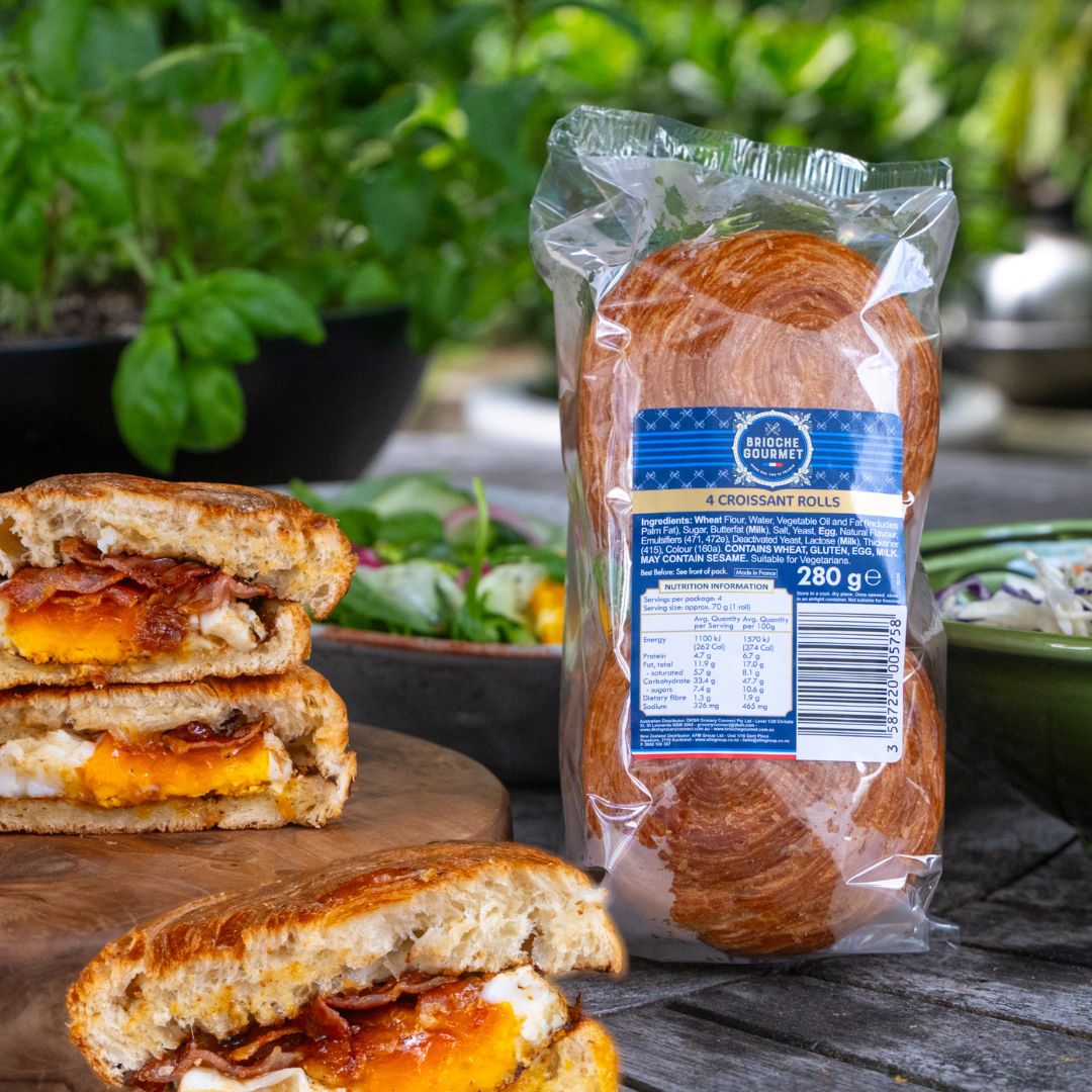 An outdoor table with a plate of bacon butties and a packet of Brioche Gourmet Croissant Rolls