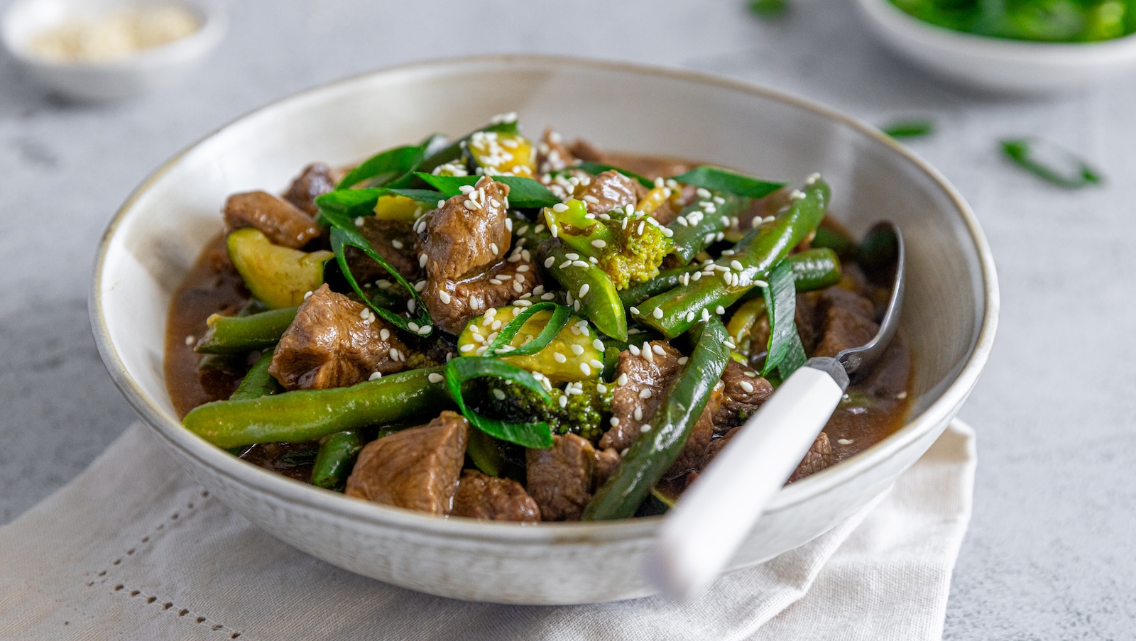 A white bowl of saucy stri fry lamb with green vegetables