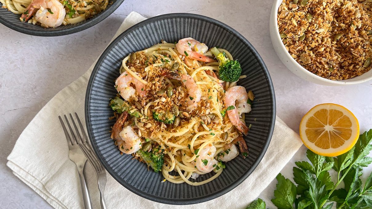 Spaghetti with prawns and broccoli and brown crumbs on top.