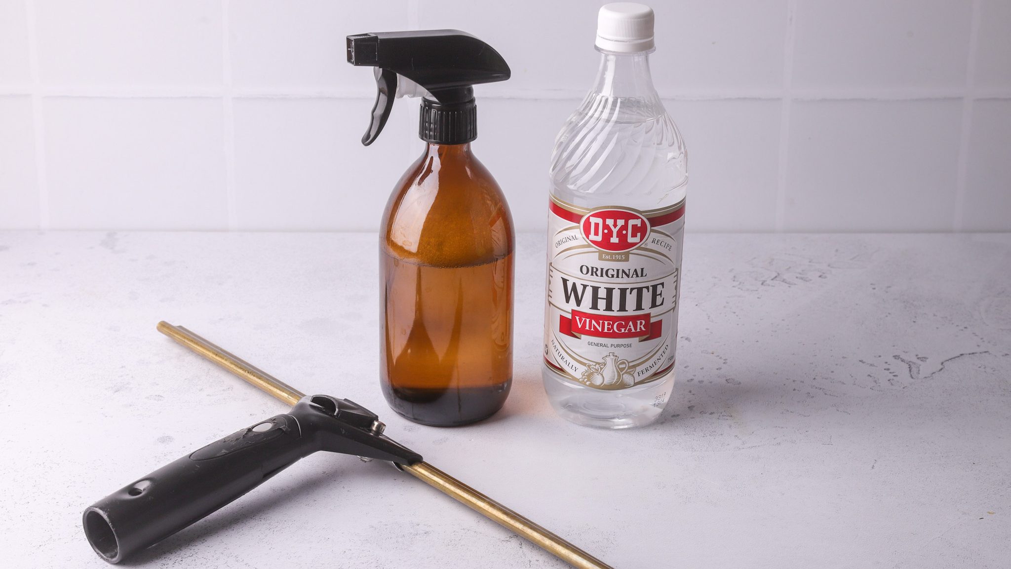 A brown spray bottle, a bottle of vinegar and a glass squeezer on white surface.