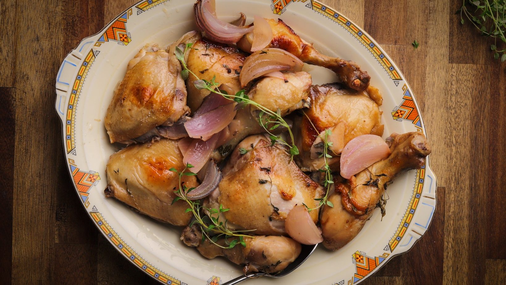 Cooked chicken pieces on a plate topped with red onion and thyme.