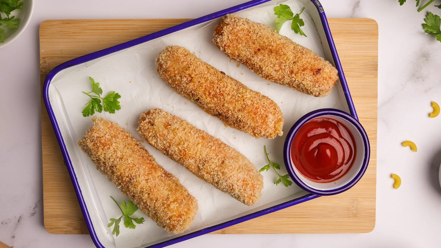 Four crumbed sausages on a white tray with a pot of tomato sauce.