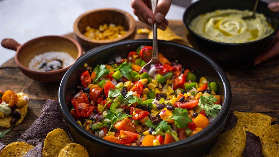 Mexican avocado salad with corn, black beans, capsicum and avocado dressing in a black bowl