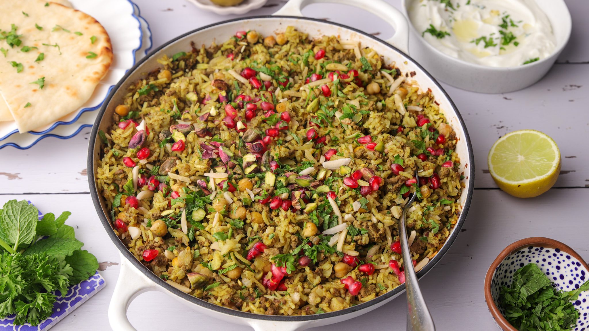 A shallow pan full of colourful rice dish with a spoon. Various ingredients around it.