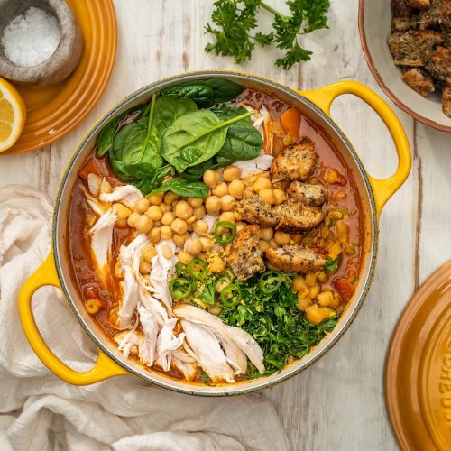 A yellow pot of soup with chicken, chickpeas, croutons and greens.