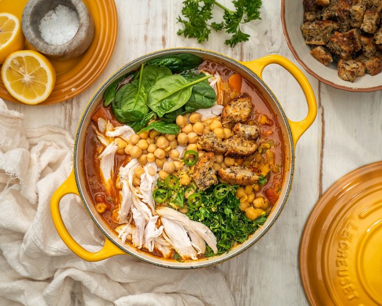A yellow pot of soup with chicken, chickpeas, croutons and greens.