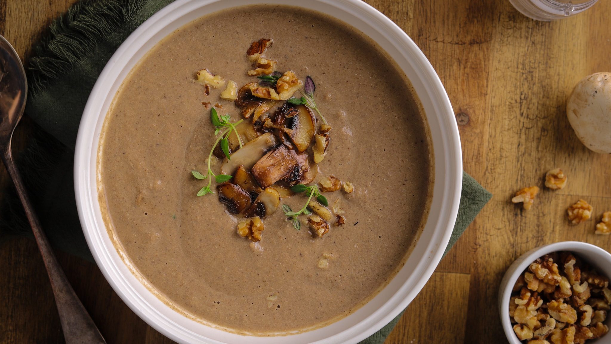 A bowl of thick brown creamy soup with mushroom slices and walnuts pieces on top.