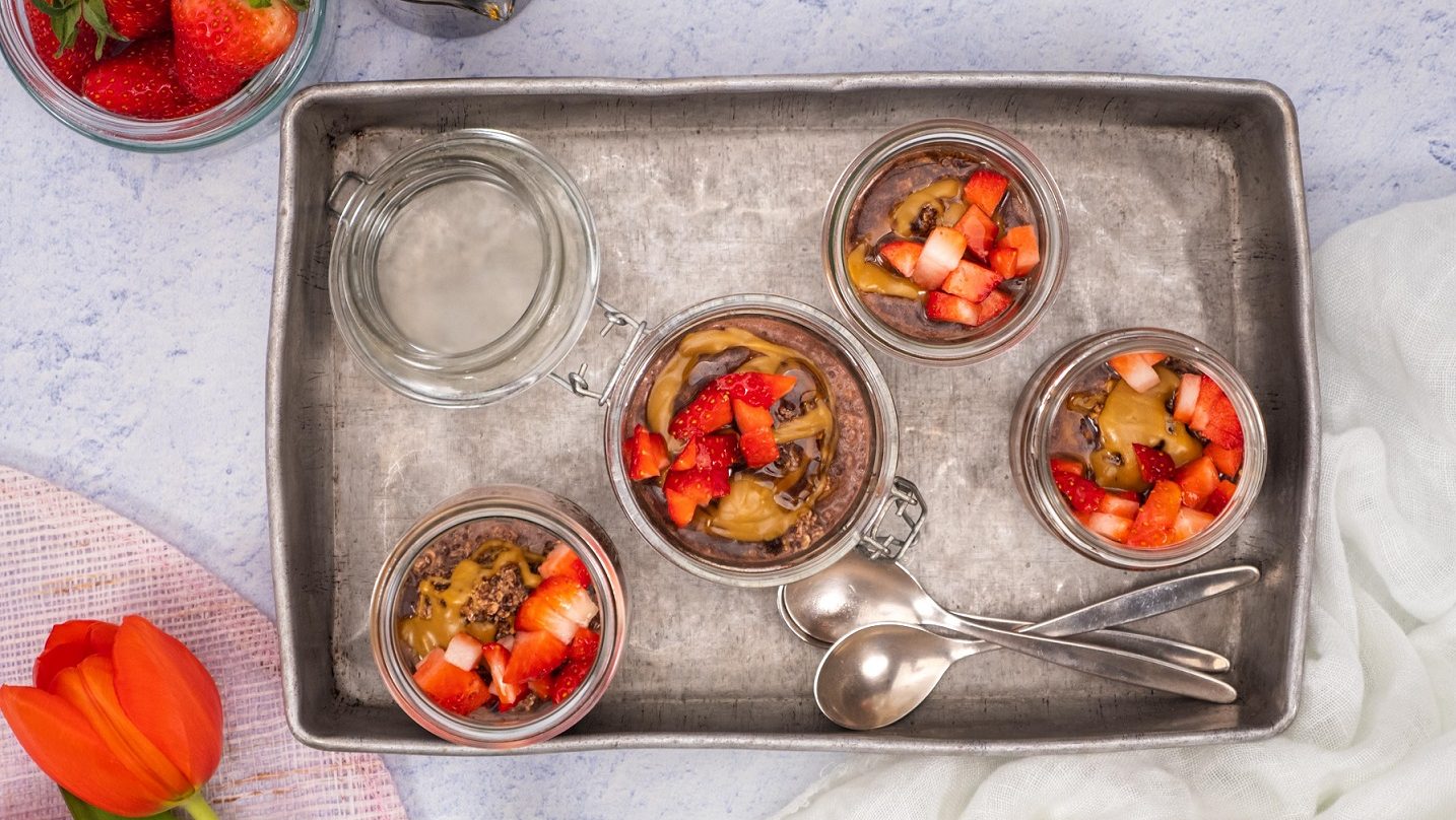 Four chocolate oat pottles presented in a tray, served in glass jars and topped with peaNOT butter and strawberries.