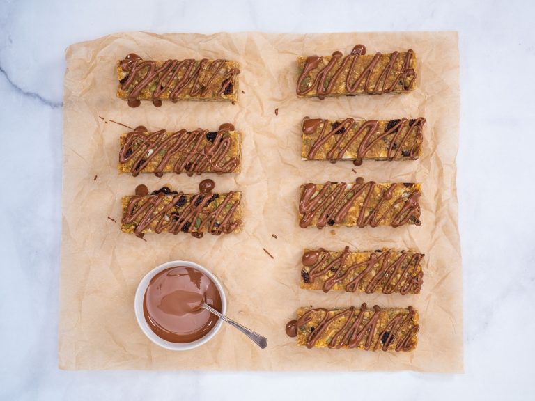 Two rows of peaNOT butter based muesli bars, nut-free and delicious, set on baking paper with a jar of chocolate sauce.