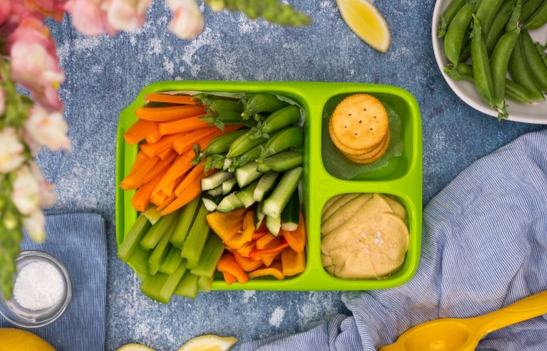 PeaNOT butter hummus, crackers and a variety of fresh vegetable sticks in a green kids' lunchbox.