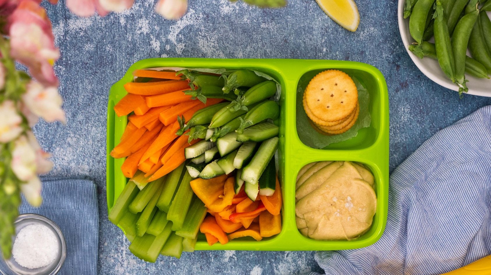 PeaNOT butter hummus, crackers and a variety of fresh vegetable sticks in a green kids' lunchbox.