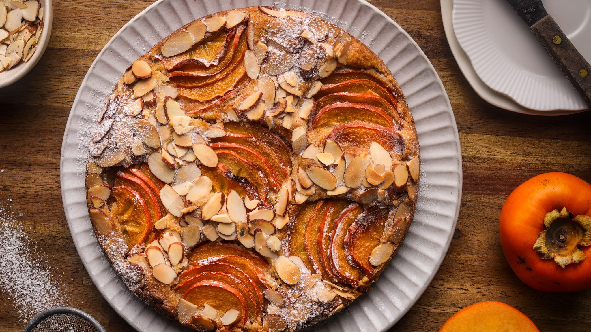 Birdseye veiw of a round cake on a plate with persimmon slices and almonds.