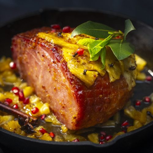 A baked ham with slices of pineapple and green leaves on top