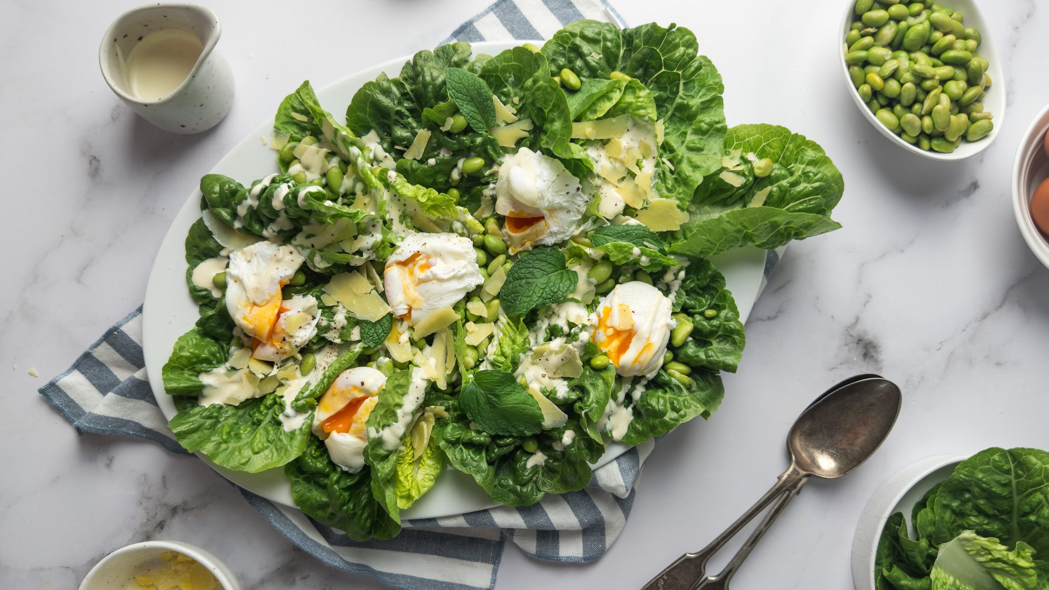 Fresh salad featuring a perfectly poached egg atop a bed of vibrant edamame, mixed greens, and fragrant mint leaves, drizzled with a light dressing