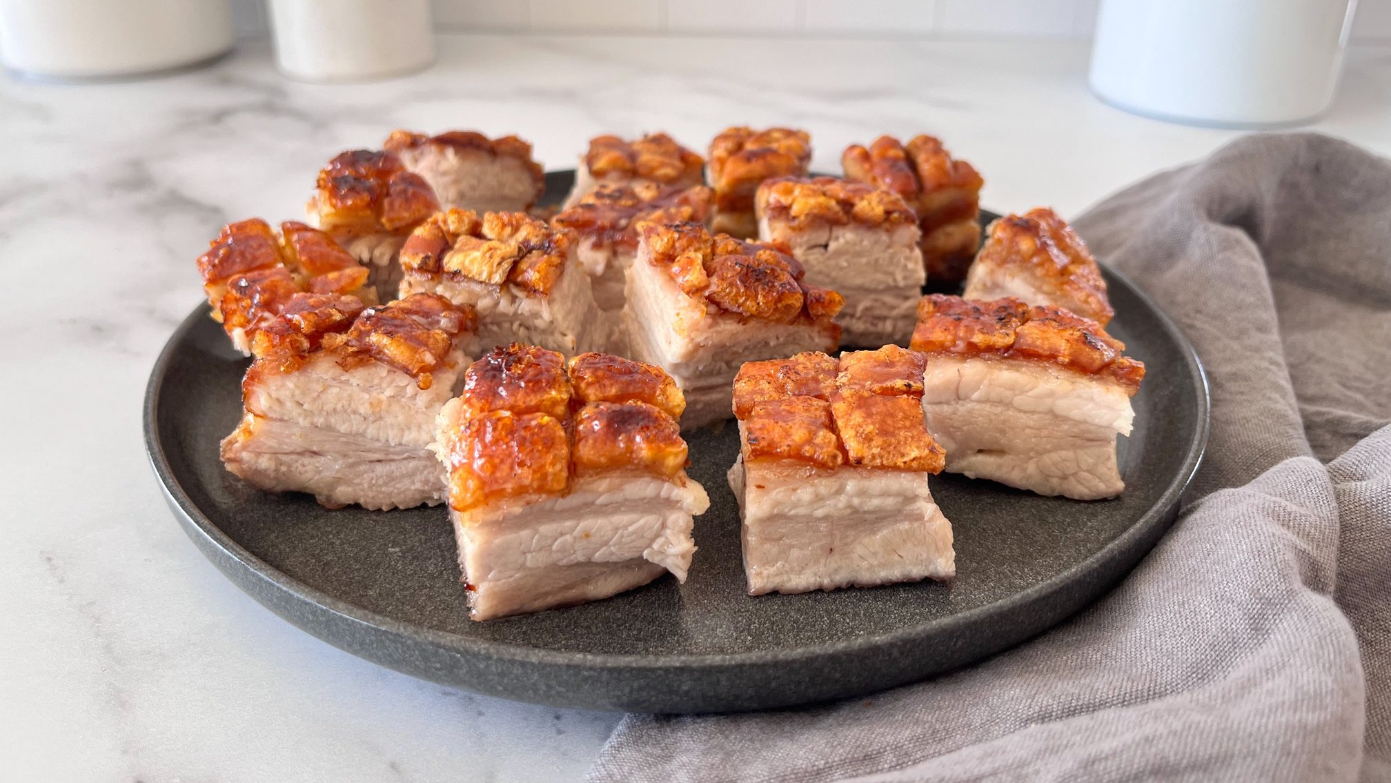 Cooked pork belly cubes with crispy brown cracklings on black plate on soft cloth.