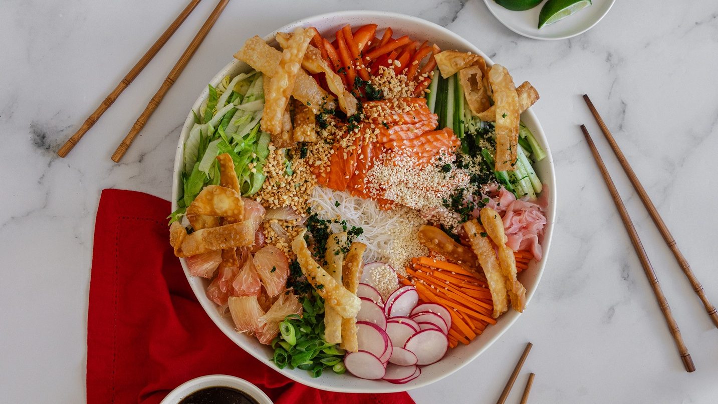 Birdseye view of colourful salad in a large round platter with raw salmon, green and red vegetables and white noodles.