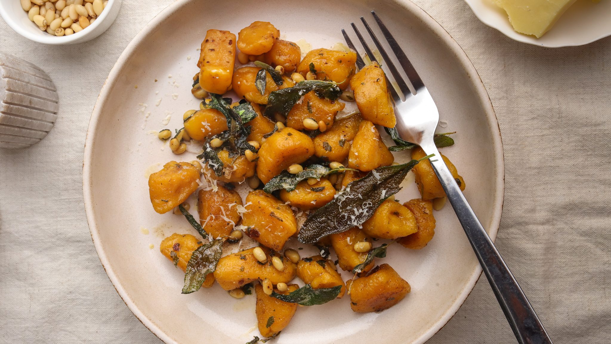 Brown gnocchi dish with wilted green and nuts on a white plate with a fork.