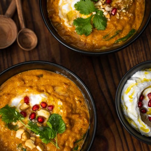 Easy weeknight meals - Two bowls of pumpkin dahl topped with white cream and red berries, and a bowl of yoghurt with red berries.