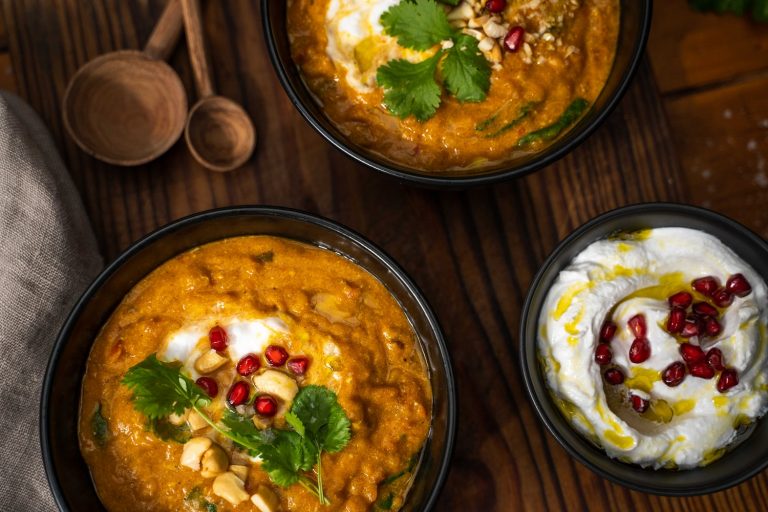 Easy weeknight meals - Two bowls of pumpkin dahl topped with white cream and red berries, and a bowl of yoghurt with red berries.