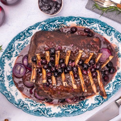 Venison rack duo crossed on a platter served with a rich whole blueberry balsamic sauce and red onions.