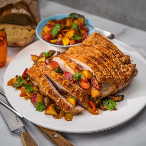 A roast pork topped with colourful fruit salsa, and a small bowl of salsa in the back
