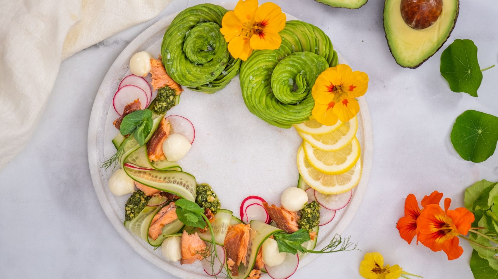 Smoked salmon wreath with highly decorative accents of edible flowers, lemon slices, fresh herbs and avocado slice spirals.