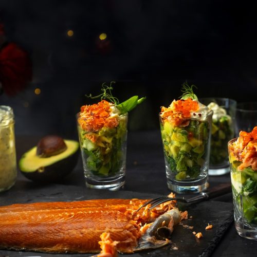A large fillet of salmon and a few glasses full of salmon and avocado cocktails
