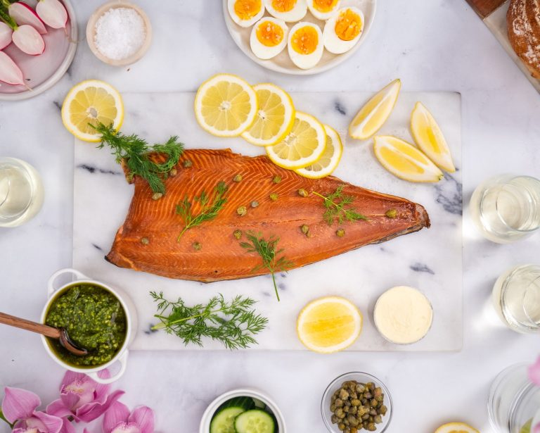 Smoked salmon side on a marble platter served with fresh dill, lemon slices, capers and a pottle of rich pesto and pine nut sauce.